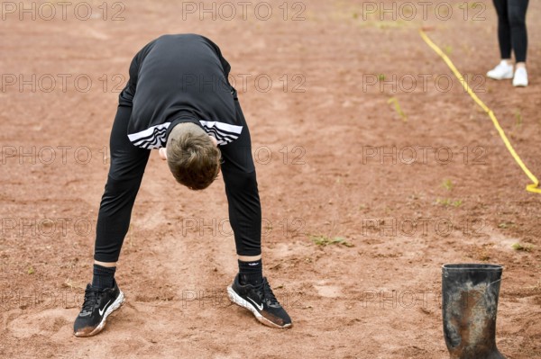 A teenager in sportswear throws a rubber boot on an ash track rubber boots long throw sports and
