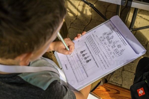 Child concentrates on a worksheet while writing, table and sunlight in the background, event for