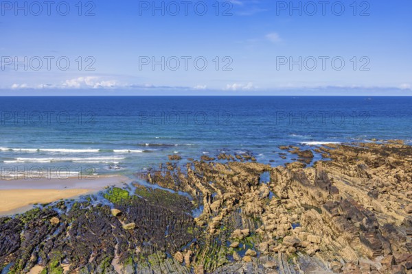 Rocky seashore in low tide with rolling sea waves and a seascape view to the horizon on a sunny