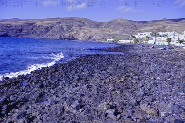 Rocky coastal landscape with blue waves and a village at the foot of the mountains under clear