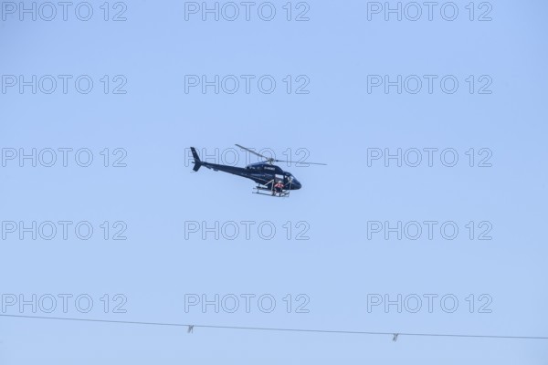 A helicopter flies over a high-voltage line in the air during technical work, Lemförde, Lower