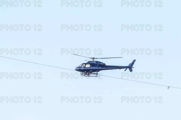 A blue helicopter flies in a clear sky. Technical details are visible, marking work on a new