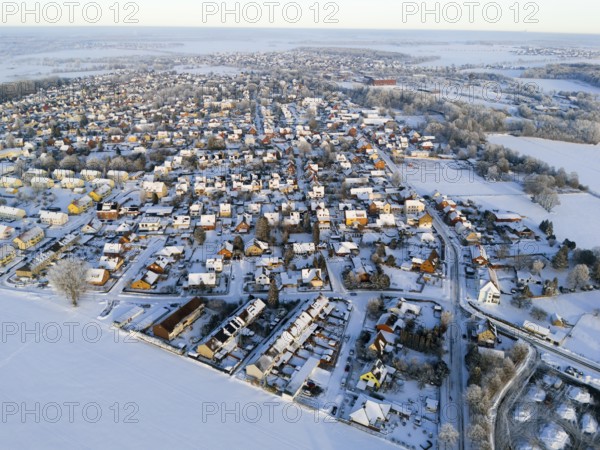Overview of a snowy village with houses and surrounding fields in the evening light, Aerial View,