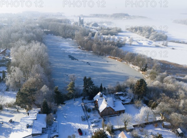 Snowy landscape with a frozen lake surrounded by trees and houses in fog, aerial view, Oelsburg,