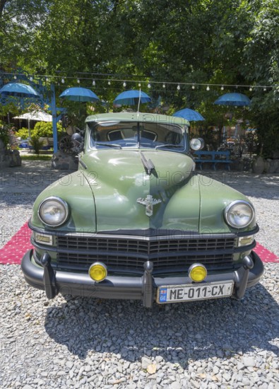 Front view of a green vintage car on a red carpet surrounded by umbrellas and pebbles, vintage car,