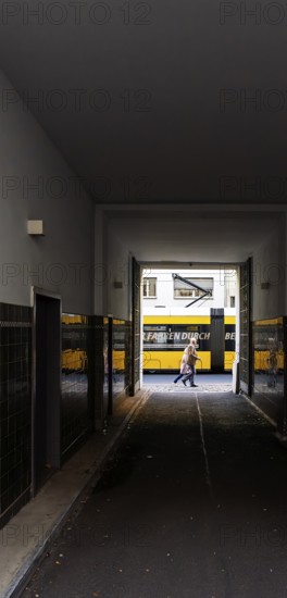 View through a corridor to the backyard onto Chässeestraße with passengers and moving tram, Berlin,