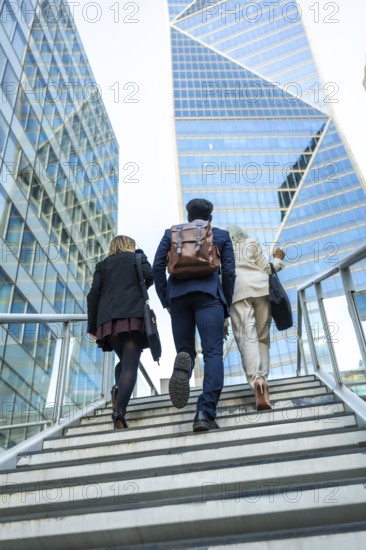 Diverse business colleagues climb a modern exterior staircase against glass skyscrapers,