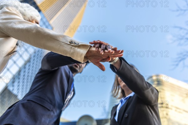Diverse business team stacking hands outdoors in an urban setting, symbolizing unity,