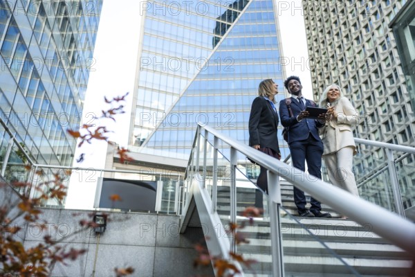 Diverse business professionals smiling and interacting while looking at a tablet on modern outdoor