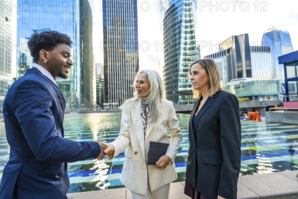 Diverse business professionals, a black man and two women, are shaking hands and discussing in a