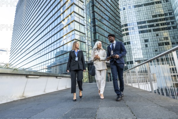 Three multi ethnic business colleagues walking and talking on a pedestrian bridge amid modern glass