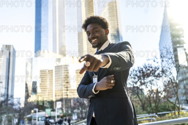 Young black businessman smiling and pointing directly towards the viewer with one hand, standing