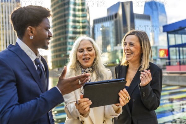 Diverse business professionals having an animated outdoor meeting, looking at a digital tablet and