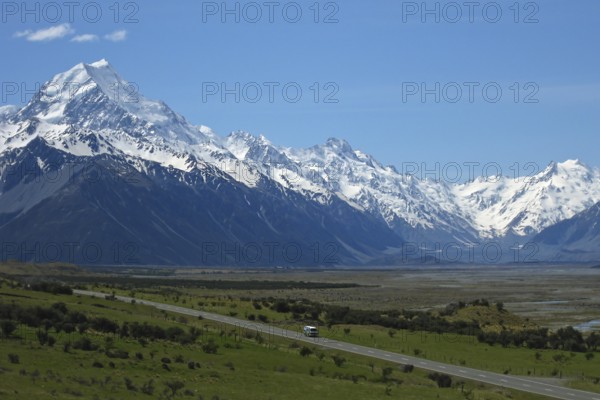 Motorhome camper van drives on a lonely country road against a huge mountain backdrop with a river