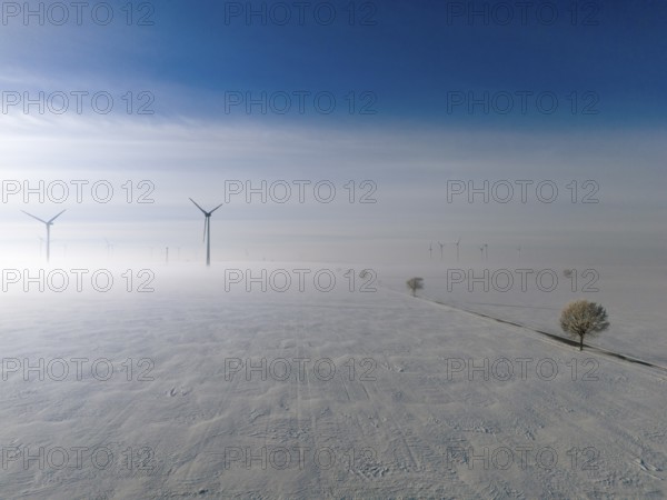 Wide snow-covered plain with wind turbines in fog under blue sky, aerial view, wind turbine and