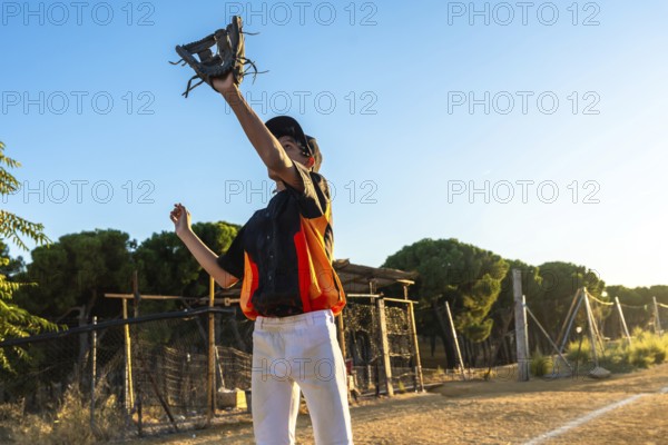 Young boy in baseball uniform and cap catches a ball with his glove on a sunny dirt field, focused