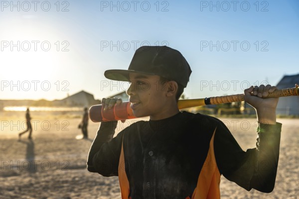 Young male baseball player holding a bat over his shoulder, wearing a cap and jersey, standing on a