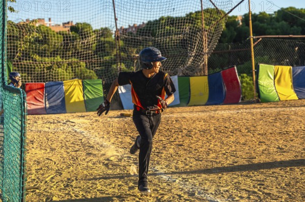 Young baseball player, wearing a helmet and uniform, running with determination on the dirt field