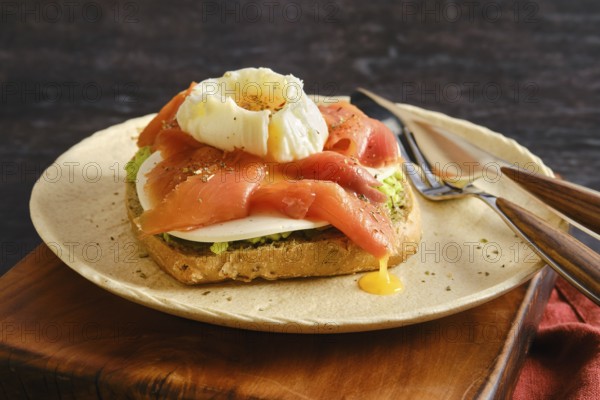A plate holds a piece of toast topped with sliced smoked salmon and a poached egg. Yellow yolk runs