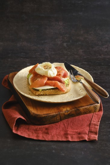 Sandwich with avocado and goat cheese topped with smoked salmon and a poached egg. The plate sits