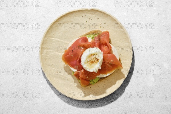 A piece of bread with avocado topped with smoked salmon, a poached egg, and seasoning on a light