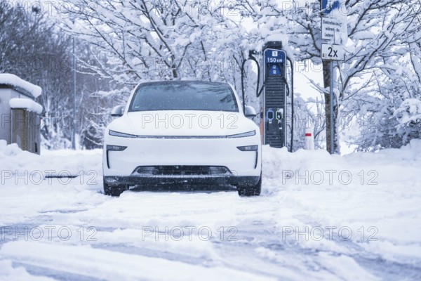 An electric car is parked in a snowy winter landscape next to a charging station, Tesla Model Y