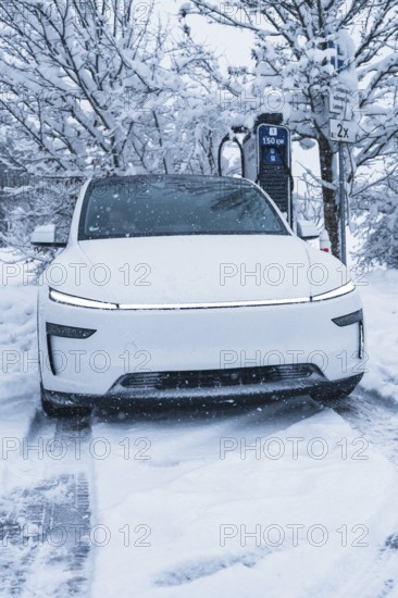 White electric car charging at a charging station in a snowy winter landscape, Tesla Model Y