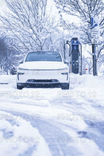 An electric car is parked on a snowy road next to a charging station, Tesla Model Y electric car,