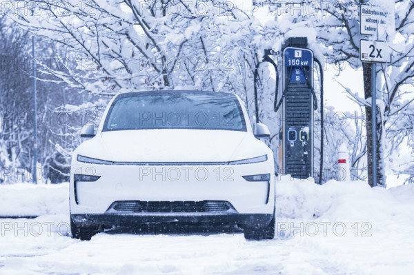 An electric car parked in the snow, close-up of the charging station in the background, Tesla Model