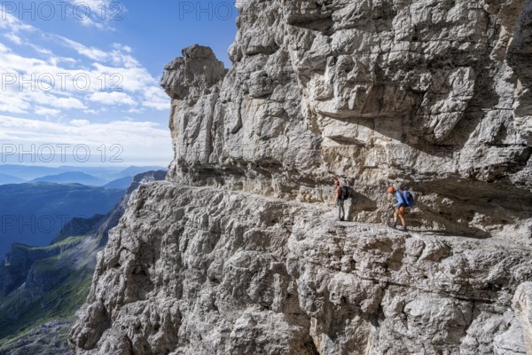 Two mountaineers on an exposed rock band in the secured via ferrata Bocciere Centrale, Brenta