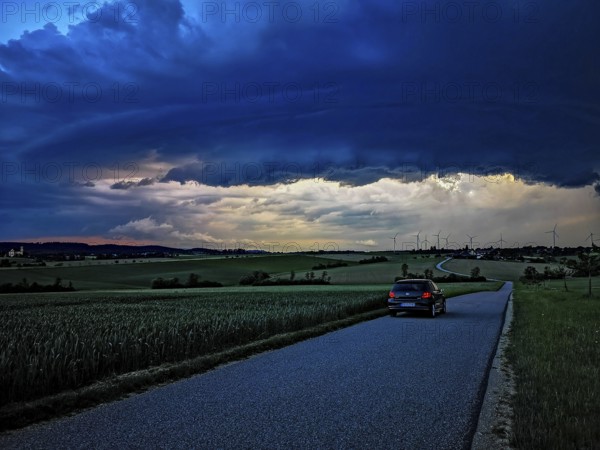 Supercell, car driving on a small road towards an approaching thunderstorm, impressive and