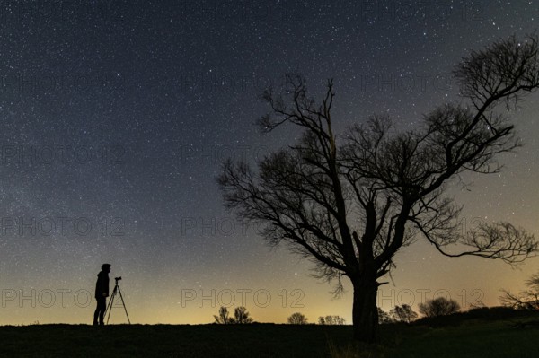 Photographer in front of a tree on the Hunte dyke in Ochsenmoor am Dümmer at night with stars,