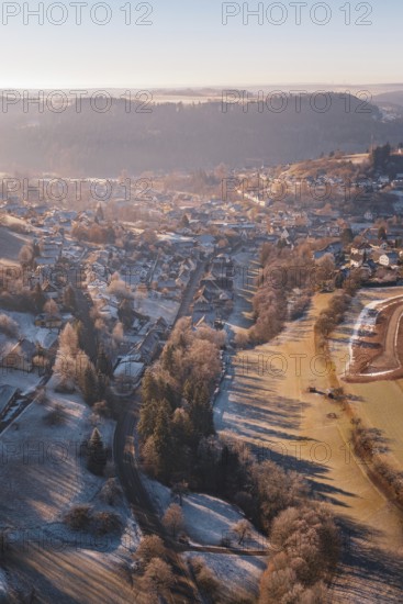Aerial view of a snowy village in a hilly landscape at sunrise with long shadow plays, Glatten,