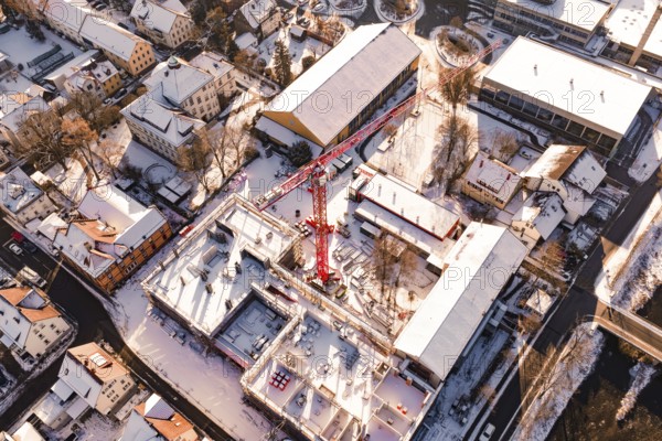 Bird's eye view of snow-covered city with construction crane and surrounding buildings in warm