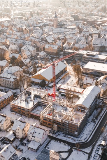 City view in winter with snow-covered roofs and a red construction crane in front of a snowy