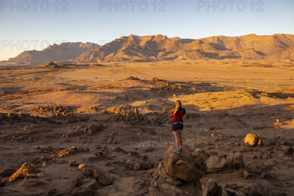Young woman standing in desert landscape with Brandberg in morning light, at sunrise, Erongo,