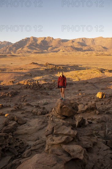 Young woman standing in desert landscape with Brandberg in morning light, at sunrise, Erongo,