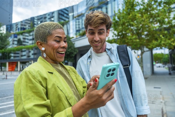 Diverse colleagues standing in a city, happily sharing and viewing content on a smartphone,