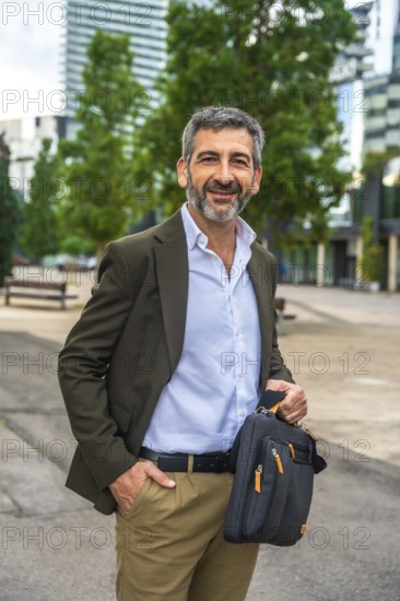 Confident mature businessman with beard and suit jacket smiling at camera, holding a messenger bag
