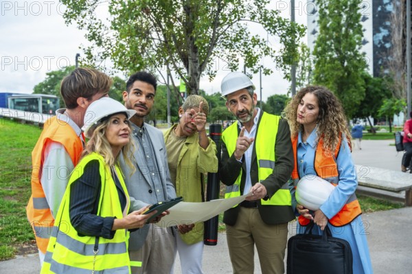 Architects, engineers, and construction colleagues in hard hats and vests discussing blueprints and