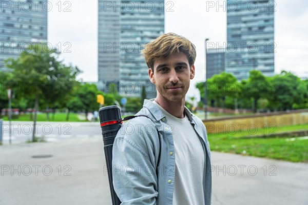 Young male architect standing outdoors with a blueprint tube, smiling confidently at the camera