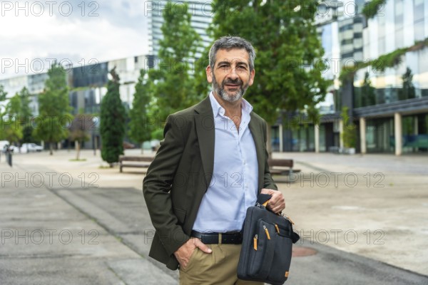 Confident mature businessman carrying a briefcase and smiling at the camera, standing outdoors with
