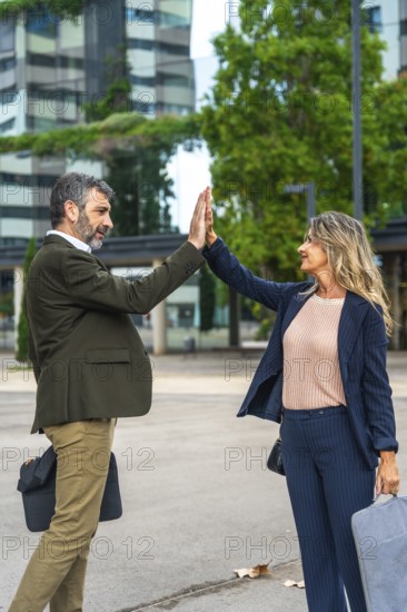 Two mature business professionals celebrating their teamwork and success with a high five, standing