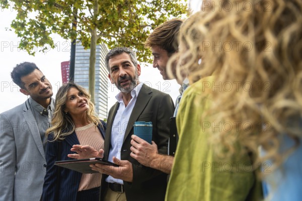 Diverse group of business professionals meeting outdoors, discussing data on a digital tablet,