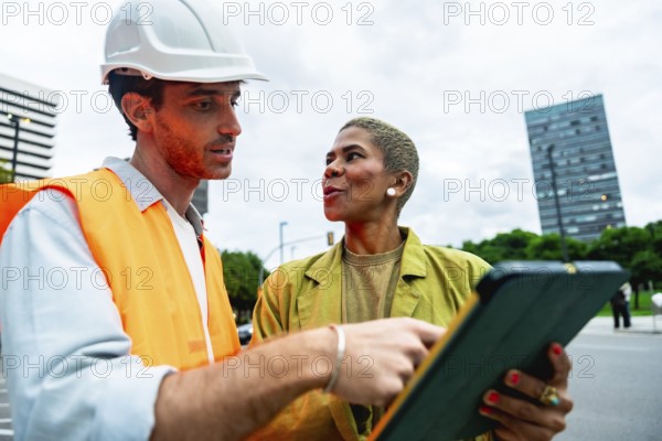Construction engineer wearing a hard hat and safety vest pointing to a digital tablet while having