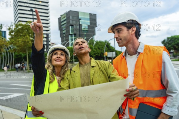 Diverse team of architects and engineers wearing hard hats and safety vests, examining blueprints