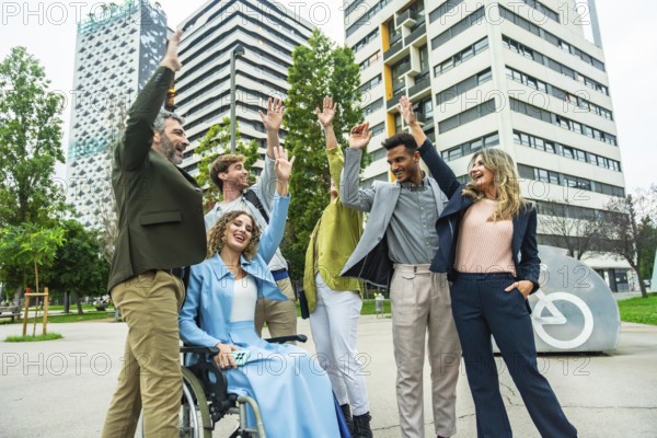 Mixed age businesspeople with a woman in a wheelchair raising their hands in celebration, showing