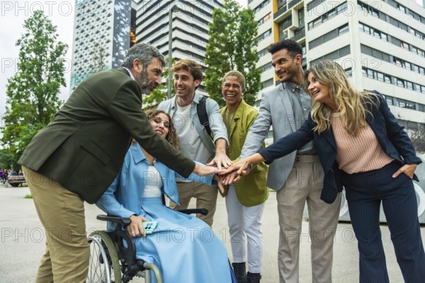 Diverse group of smiling business professionals and an executive in a wheelchair stacking hands,