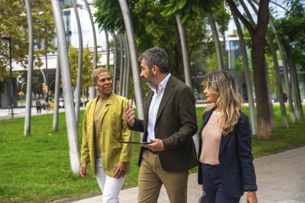 Three diverse business colleagues walking together in an urban park, engaging in a lively outdoor