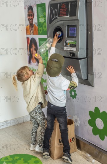 Two children, 5 and 7 years old, earn pocket money by recycling cans in a recycling machine in